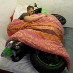 a man laying on top of a motorcycle covered in a blanket