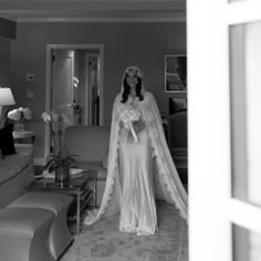 black and white photograph of woman in bridal gown with veil over head standing in living room