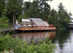 a dock with tables and umbrellas on it next to the water in front of some trees