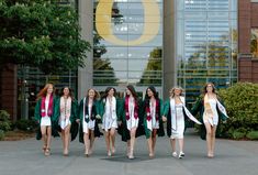 a group of women in graduation gowns walking down the street with their arms around each other