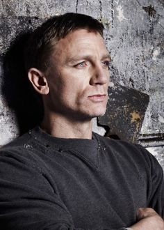 a man leaning against a wall with his arms crossed and looking off to the side