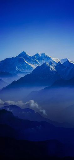 the mountains are covered in clouds and blue hues as seen from an airplane window