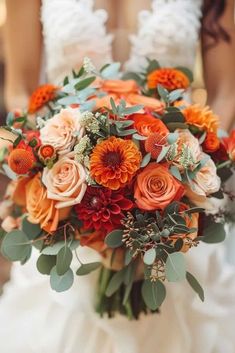 a bridal bouquet with orange and red flowers in the bride's dress at her wedding