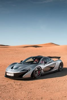 a silver sports car parked in the middle of a desert area with sand dunes behind it