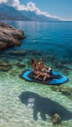 two women are on a jet ski in the clear blue water near some rocks and an island