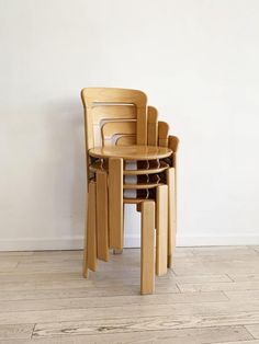 three chairs stacked on top of each other in front of a white wall and wooden floor