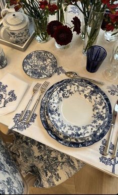 blue and white dinnerware set on a table with red flowers in vases behind it