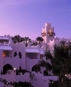 a large white building with a clock on it's side and palm trees in the foreground