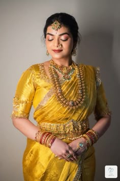 a woman in a yellow sari with jewelry on her neck and hands behind her back