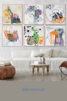 a living room filled with white furniture and paintings on the wall above it's coffee table