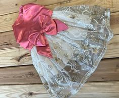 a pink and white dress with a large bow on it's headband sitting on top of a wooden floor