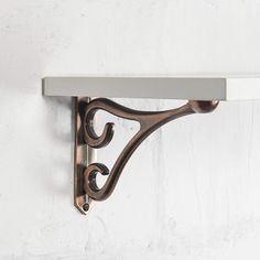 a metal shelf on the wall with white painted walls behind it and an ornate design