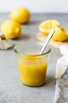 a glass jar filled with yellow liquid next to sliced lemons and garlic on a cutting board