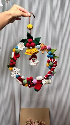 a person is holding up a christmas wreath made out of knitted toys and yarn