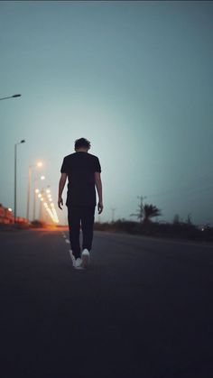 a man walking down the street at night with his back to the camera and lights on