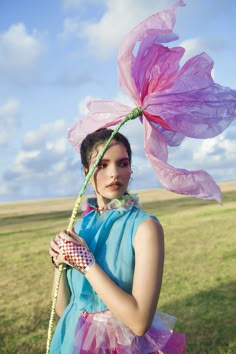 a woman in a blue dress and pink flower headdress holding a green stick