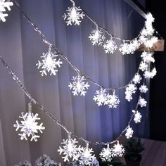 snowflake lights are hanging from the ceiling in front of a curtained window