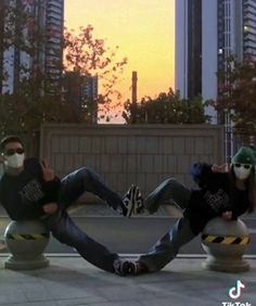 two people sitting on top of cement balls in the middle of a city at sunset