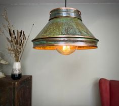 a lamp hanging from the ceiling next to a red chair and vase with dried flowers