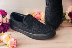 a pair of black slip ons next to flowers