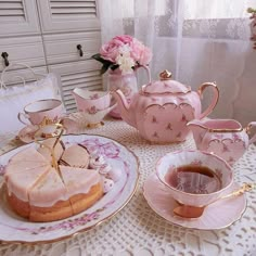 a table topped with pink tea cups and saucers next to a cake covered in frosting