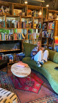 a woman sitting on top of a green couch next to a fire place in a living room