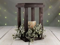 a candle in a wooden lantern holder with greenery