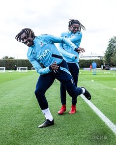 two soccer players in blue uniforms are playing on the field with their arms around each other