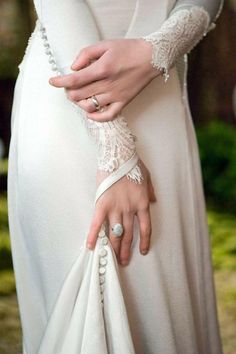 a woman in a white dress is holding a wedding ring on her hand and wearing a lace bracelet