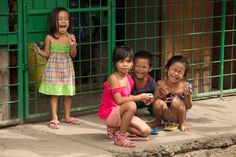 three young children sitting on the ground in front of a green gate with their mouths open