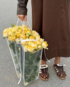 a person holding a clear bag with yellow roses in it and leopard print slippers