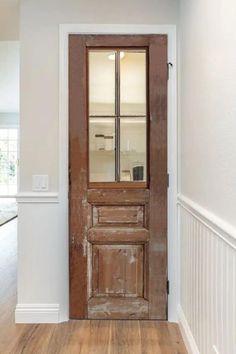 an old wooden door with glass is in the middle of a white wall and hardwood floor