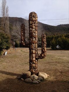 a large cactus sculpture sitting in the middle of a field next to rocks and trees