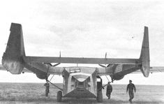 two men walking towards an old airplane on the ground with it's wings open