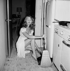 a woman sitting on the floor with a broom in front of an oven and refrigerator