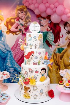 there is a white cake with princesses on it and balloons in the back ground