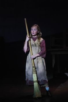 a woman holding a broom standing in the dark with her hand on top of it