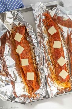 two hotdogs covered in cheese and seasoning sitting on tin foil, ready to be cooked