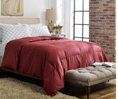 a bed with red comforter and pillows in a bedroom next to a brick wall