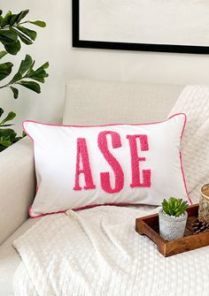 a white couch with a pink and red pillow on top of it next to a potted plant