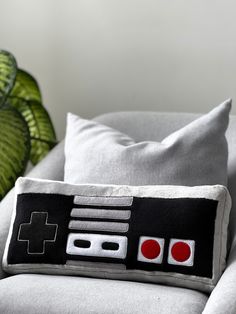 a pillow with a video game controller on it sitting on a couch next to a green plant