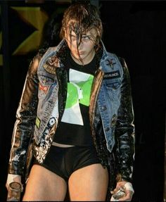 a woman with wet hair wearing black shorts and a jean jacket on her shoulders, standing in front of a stage backdrop