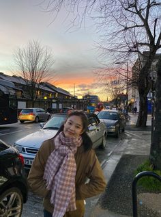 a woman is standing on the sidewalk with her scarf around her neck and looking at the camera