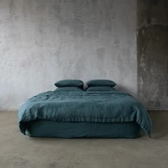 a bed with two pillows on top of it in front of a concrete wall and floor