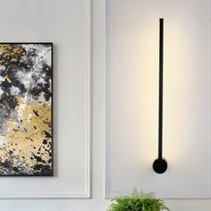 a wall mounted light next to a potted plant in a white room with gold and black accents