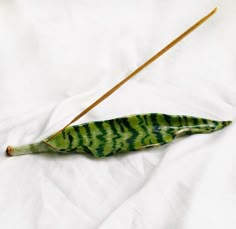 a green and black leaf with two sticks sticking out of it on a white sheet