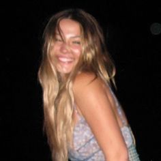 a woman with long blonde hair is smiling at the camera while wearing a blue and white tank top