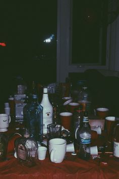 a table topped with lots of bottles and glasses on top of a red cloth covered table