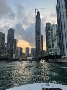 the sun is setting in front of some tall buildings on the water with boats passing by