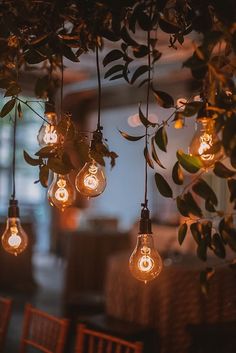 several light bulbs hanging from the ceiling in a room with wooden chairs and tablecloths